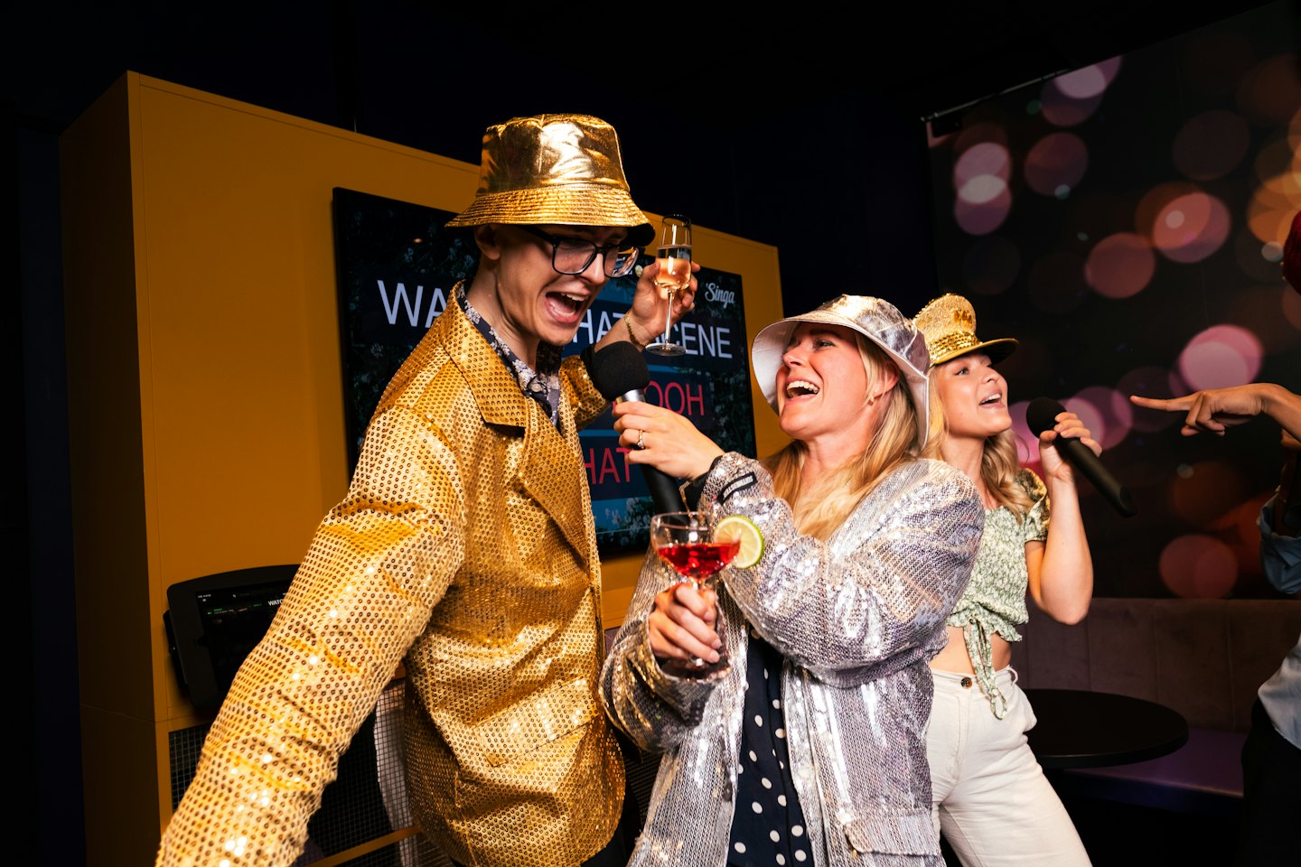 Przyjaciele śpiewający karaoke w świątecznych strojach i z drinkami.